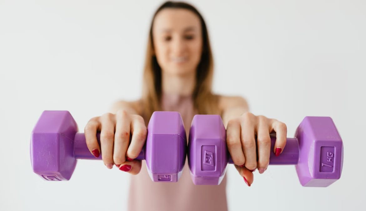 Defocused content young female doing bicep exercise with dumbbells during functional training in light studio